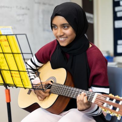 Girl playing a guitar. She has a smile across her face